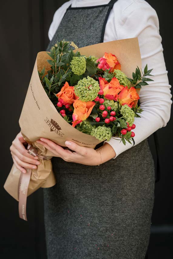 Floral Designer Frida's tiene in mano Bouquet Vitaminico di rose arancio, viburno e iperico
