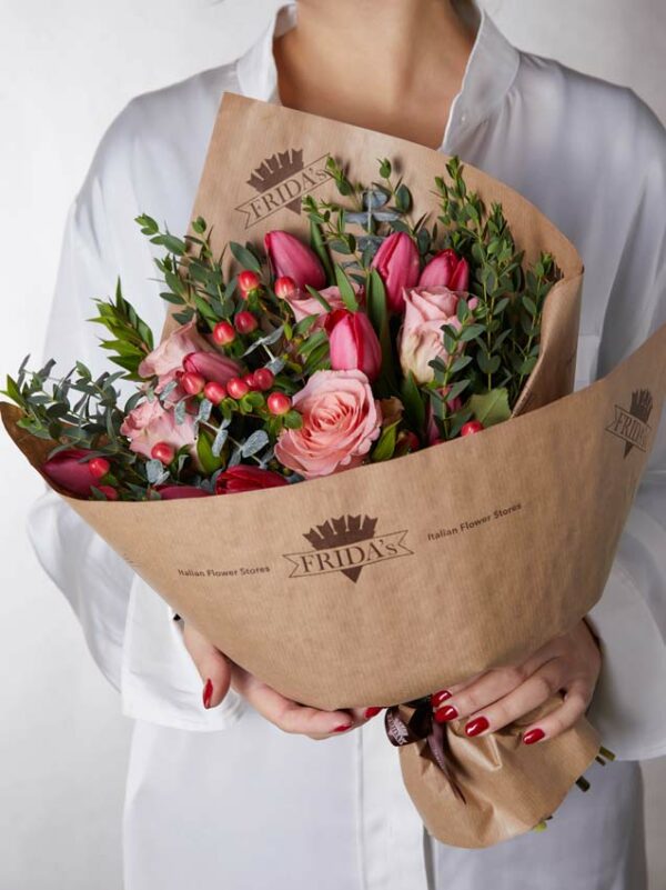 Bouquet Ginevra, mazzo di fiori incartato con tulipani rossi e rose rosa. Ragazza con camicia bianca tiene in mano un bouquet di fiori con incarto Frida's