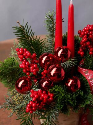 Centrotavola Merry Xmas, composizione di conifere con candele rosse, ilex e decorazioni natalizie