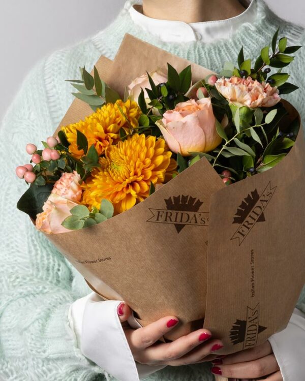 Bouquet Tangerine, mazzo di fiori incartato con Rose rosa, crisantemi arancioni, garofani arancio, iperico rosa e verde di stagione. Ragazza tiene in mano un bouquet di fiori con incarto Frida's