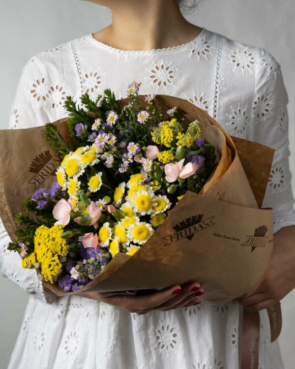 Ragazza tiene tra le mani Bouquet Fiori di Campo, bouquet di crisantemini bianchi e gialli, achillea gialla, statice, lavanda, aster, solomio e verde di stagione con incarto Frida's